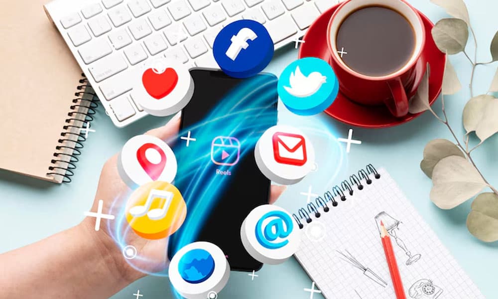 Social media icons floating around smartphone on workspace with coffee and stationery; digital marketing concept.